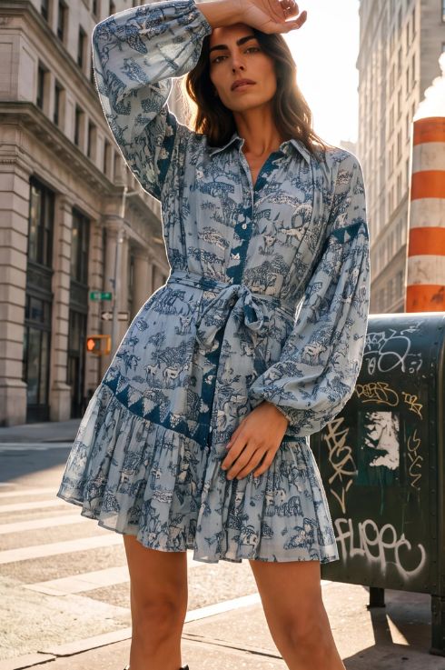Robe courte bohème bleu clair à imprimé style toile de Jouy, col chemise et ceinture nouée, portée dans une rue de New York