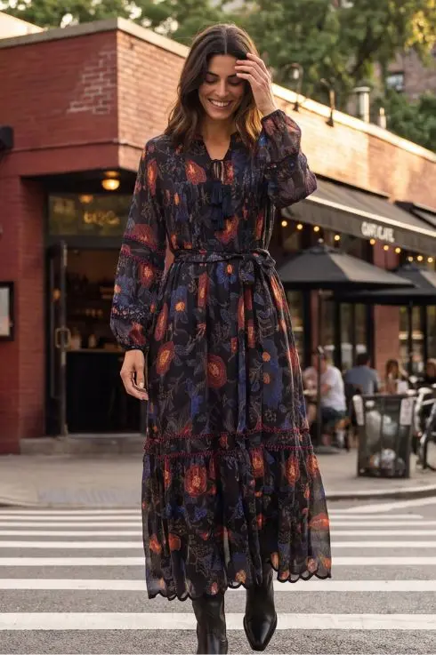 Robe longue bohème noire à imprimé floral rouge et bleu, col à pompon, ceinturée et volantée, portée avec des bottes noires à New York