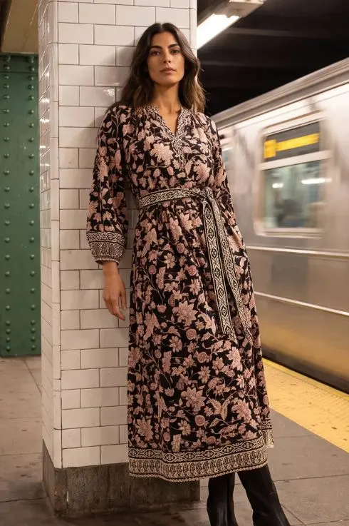 Robe longue bohème noire à imprimé floral rose poudré, ceinture tissée et bordure brodée, portée avec des bottes noires dans le métro de New York