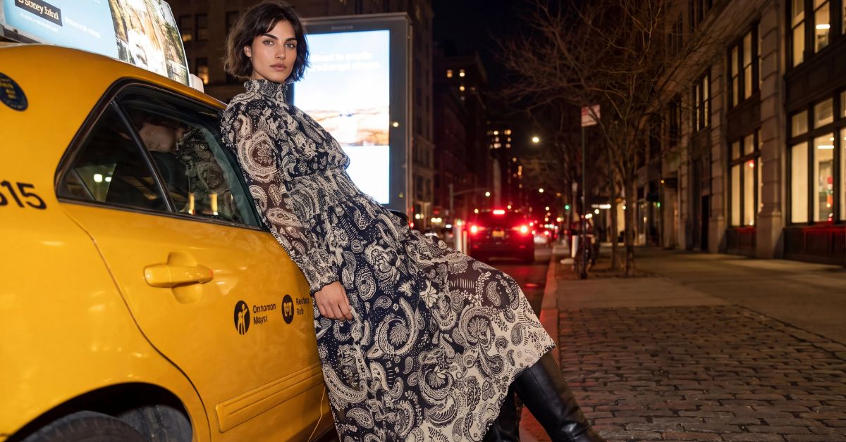 Robe longue bohème à imprimé paisley marine et écru, col montant, portée avec des bottes hautes contre un taxi jaune de nuit à New York